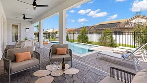 Un patio techado con mobiliario exterior, piscina y vista a un barrio residencial.