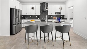 Una cocina moderna con armarios blancos, un refrigerador de acero inoxidable, una isla central con taburetes y un salpicadero de azulejos negros.