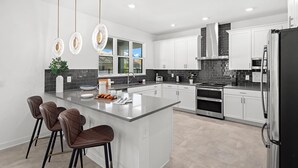 A modern kitchen with a central island, white cabinetry, stainless steel appliances, and pendant lighting.