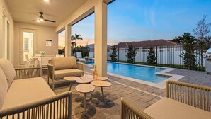 A poolside area with a sofa, chairs, and round tables.