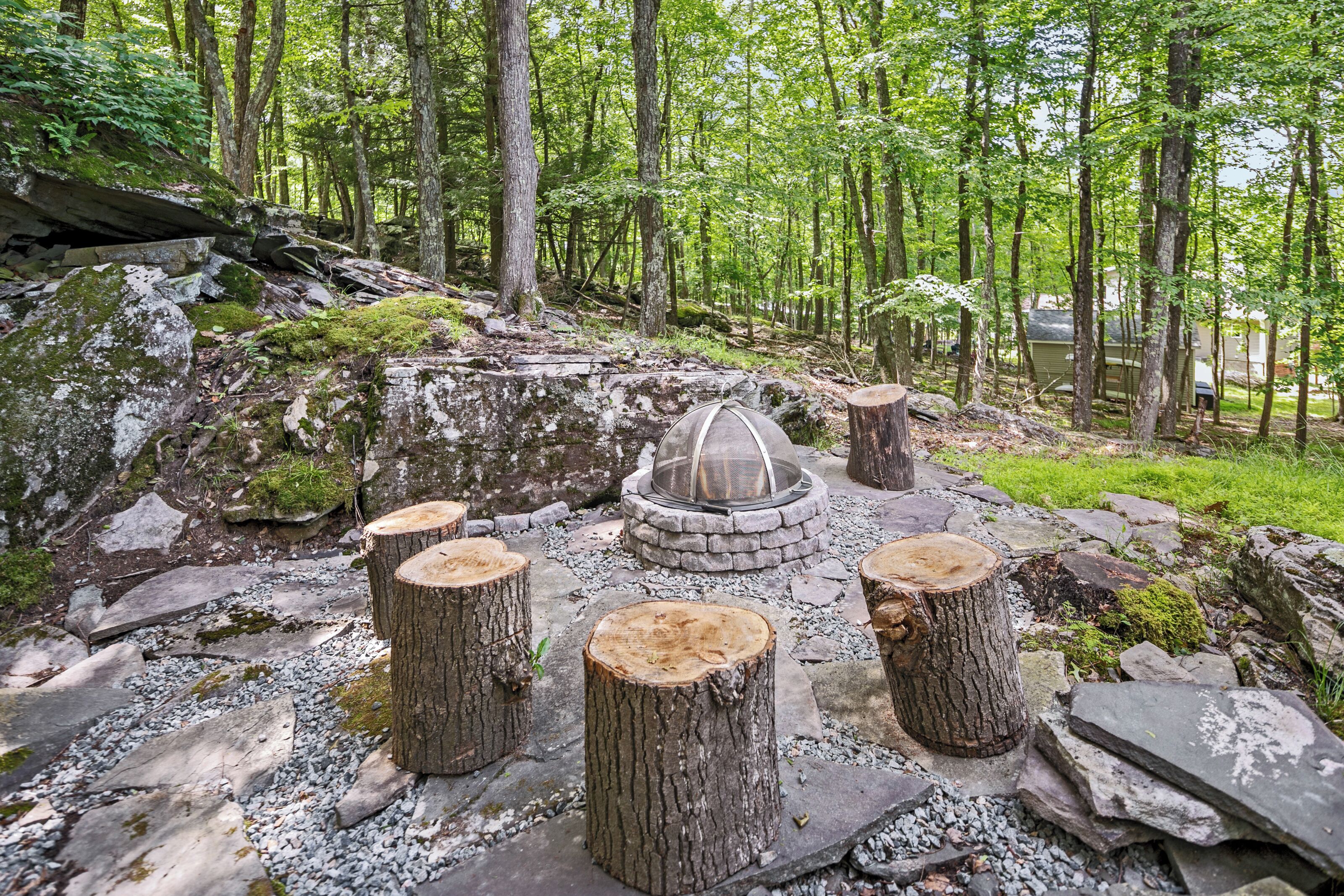 Un hogar de piedra rodeado de troncos de madera en un entorno forestal.