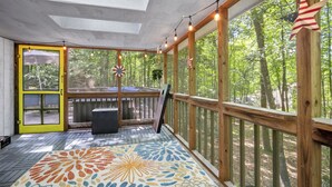A covered deck with a colorful floor pattern, wooden railings, and a view of a forest. - Eclectic Family Poconos Escape! Skiing 5min away! Firepit, Near Woodloch/winery! (Lackawaxen)