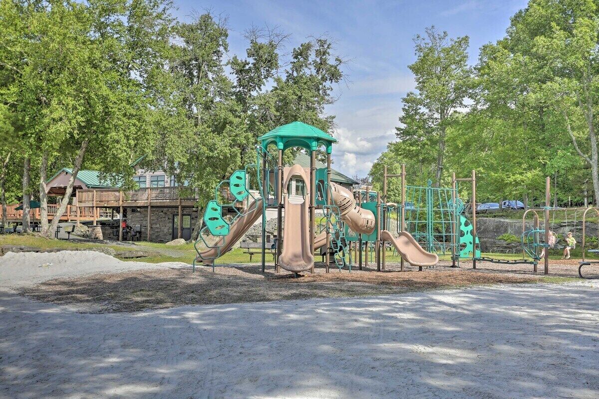 A playground with various play structures, including slides and climbing areas, surrounded by trees and a building in the background.
