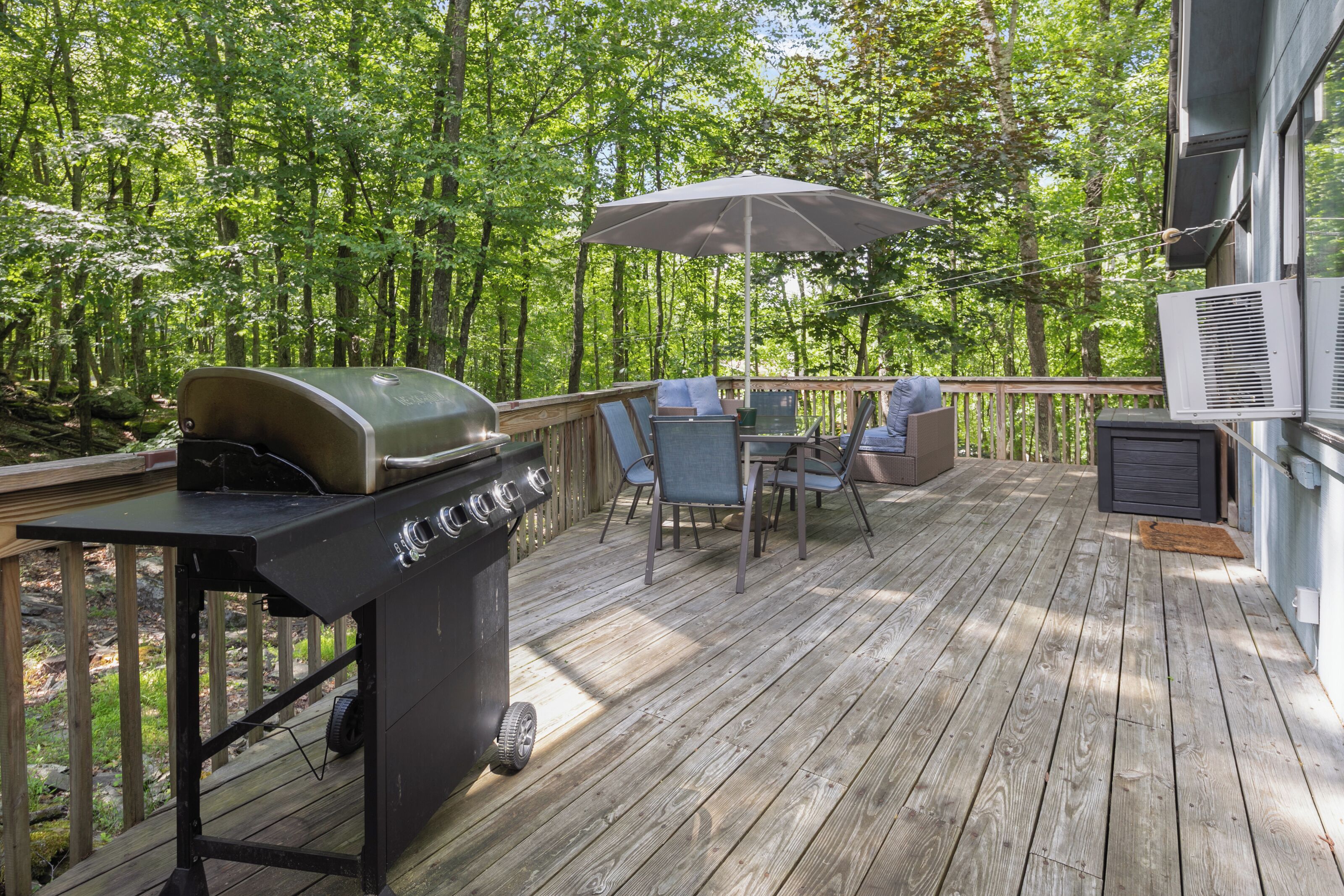 A wooden deck with a grill, outdoor furniture, and a view of a forest.