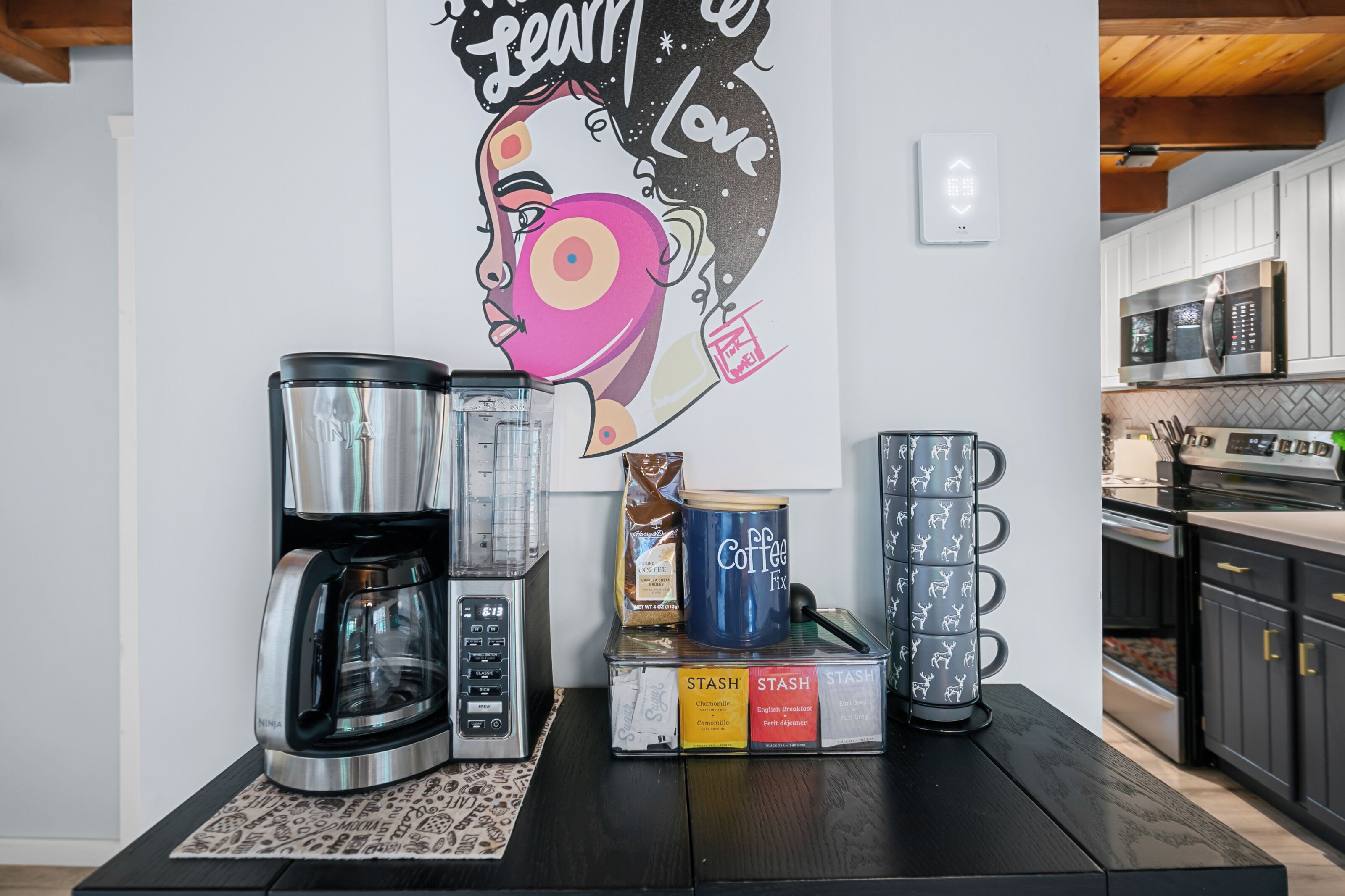 Una cocina con cafetera, molinillo de café y una taza sobre una mesa.