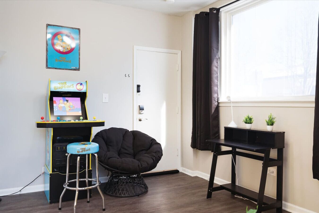 A room with a black bean bag chair, a small table with plants, a wall-mounted TV, and a door.
