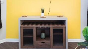 A room with a yellow wall, a mounted TV, a wooden console table with a plant, and a small cabinet.