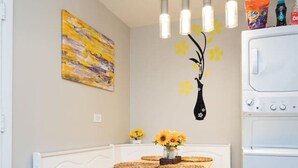 Eine Küche mit einer weißen Arbeitsfläche, einem Tisch mit Keksen, einer Vase mit Sonnenblumen, einem Gemälde und einem weißen Kühlschrank.