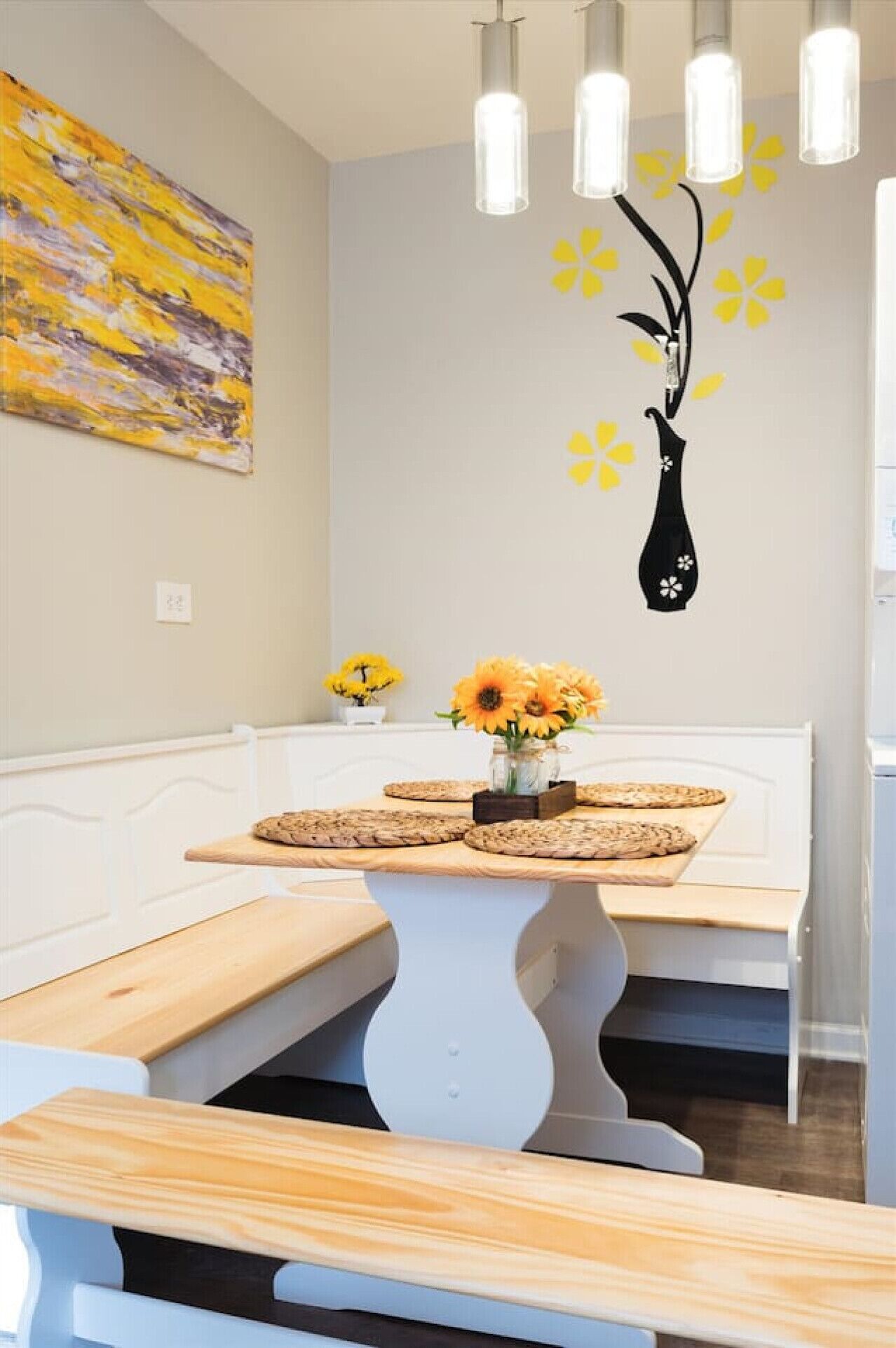 A modern interior with a bench, a table with cookies, a vase with flowers, and a wall with a painting and a black vase decal.