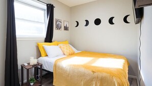Ein Schlafzimmer mit einem Bett, einem Nachttisch mit Lampe, einem Fenster mit Vorhängen und einer Wand mit Halbmond-Dekorationen.