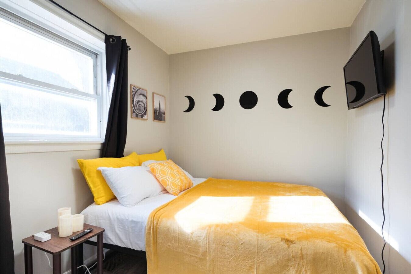 A bedroom with a bed, a nightstand, a TV, and a wall with moon phases.