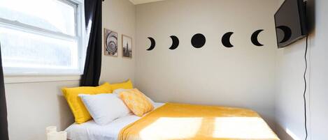A bedroom with a bed, a nightstand, a TV, and a wall with moon phases.
