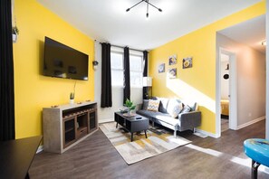 Ein Wohnzimmer mit einem Flachbildfernseher, einem Sofa, einem Couchtisch und einer Treppe, die in einen anderen Raum führt.