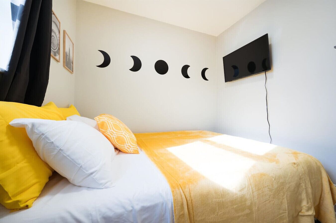A bed with yellow and white bedding, a wall-mounted TV, and a series of moon phases on the wall.