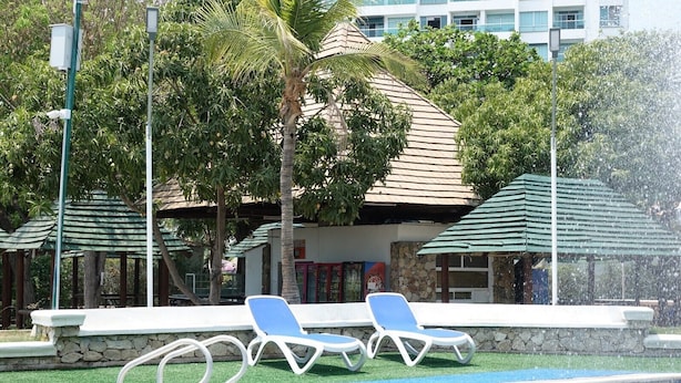 Un área de piscina con sillones de descanso, un muro de piedra y un edificio con techo de tejas al fondo.
