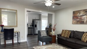 A modern living room with a dark brown sofa, a grey armchair, and a patterned rug. A ceiling fan and a large mirror are visible.