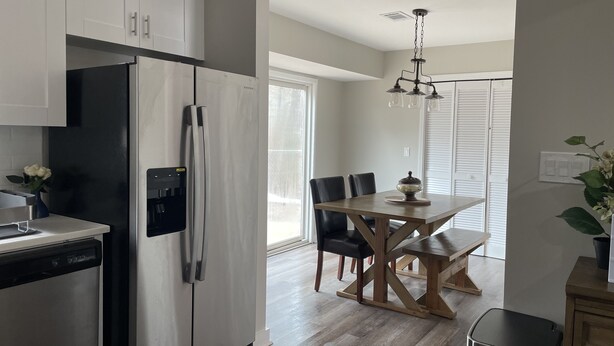 A modern kitchen with white cabinets, a stainless steel refrigerator, and a wooden dining table with chairs.