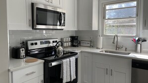 A modern kitchen with white cabinetry, a stainless steel microwave, a coffee maker, and a sink with a window above it.