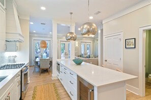A modern kitchen with white cabinets, a central island, pendant lighting, and a view to the dining area. - Wow Renovation, Nice Porches, & Tower, 4 Houses to Beach in Seaside + 2 Bikes (Seaside)
