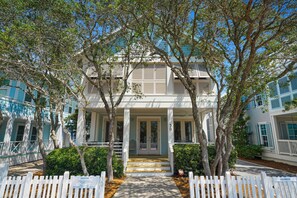 A two-story house with a porch, surrounded by trees and a white picket fence.