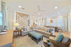 A spacious living area with a sectional sofa, a dining table, and a staircase leading to an upper level.