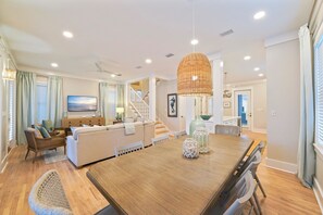 A spacious living area with a wooden dining table, a sofa set, and a staircase leading to an upper level.
