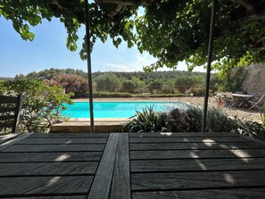 Um deck de madeira com vista para uma piscina, um jardim paisagístico e uma colina ao longe.