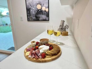 Una habitación con una encimera de mármol que presenta una tabla de embutidos, dos copas de vino blanco y un bol de nueces.