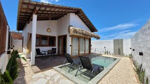 Una villa moderna con piscina, terraza de madera y estructura de techo de paja.
