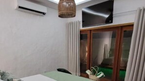 Una habitación de hotel moderna con una cama, una mesita pequeña y una silla. Se aprecia una lámpara en el techo y una ventana con cortinas.