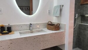 Un baño moderno con un espejo grande, un lavabo con encimera de granito, una zona de ducha y una base revestida de piedra.