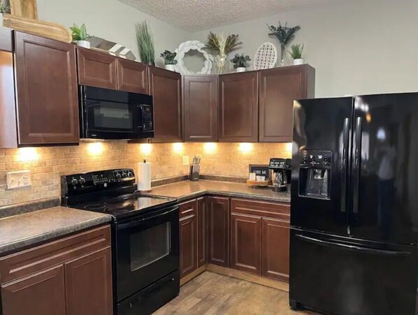 Enjoy cooking in this well-equipped kitchen with a black stove, refrigerator, and microwave, along with ample countertop space.