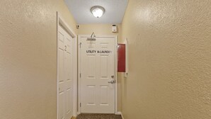 Pasillo con una puerta que dice 'UTILITY & LAUNDRY', piso cubierto de alfombra y una lámpara en el techo.