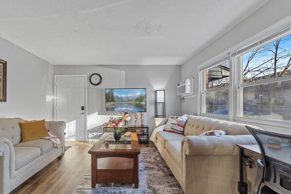 A living room with a sofa, a coffee table, a TV, and a window with a view.