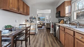 Una cocina con gabinetes de madera, una zona de comedor con mesa y sillas, un ventilador de techo y una ventana.