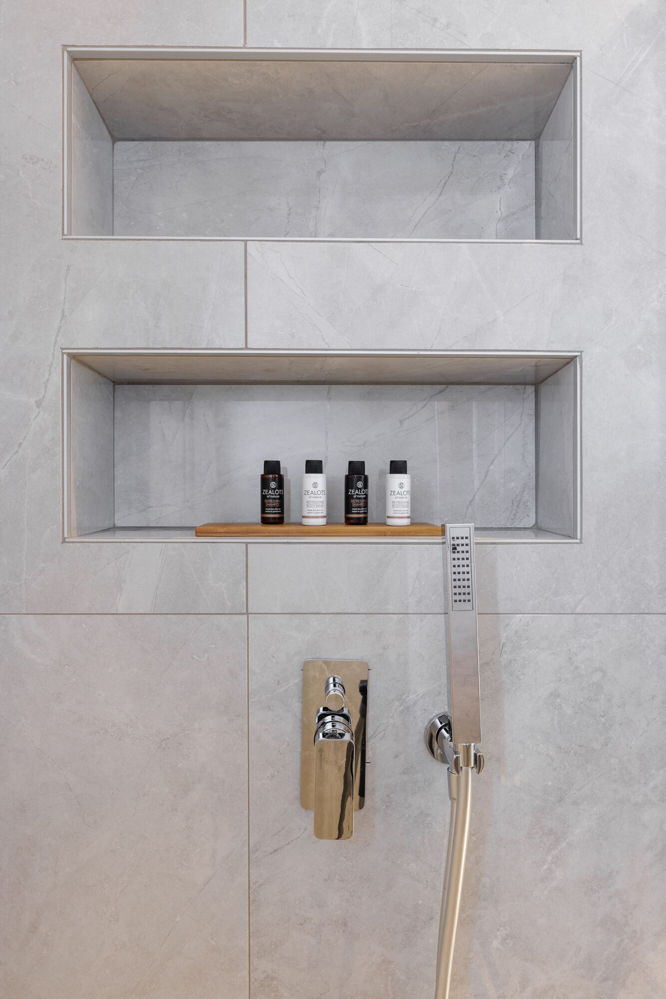A modern bathroom with a built-in shower, a wooden shelf with toiletries, and a handheld showerhead.