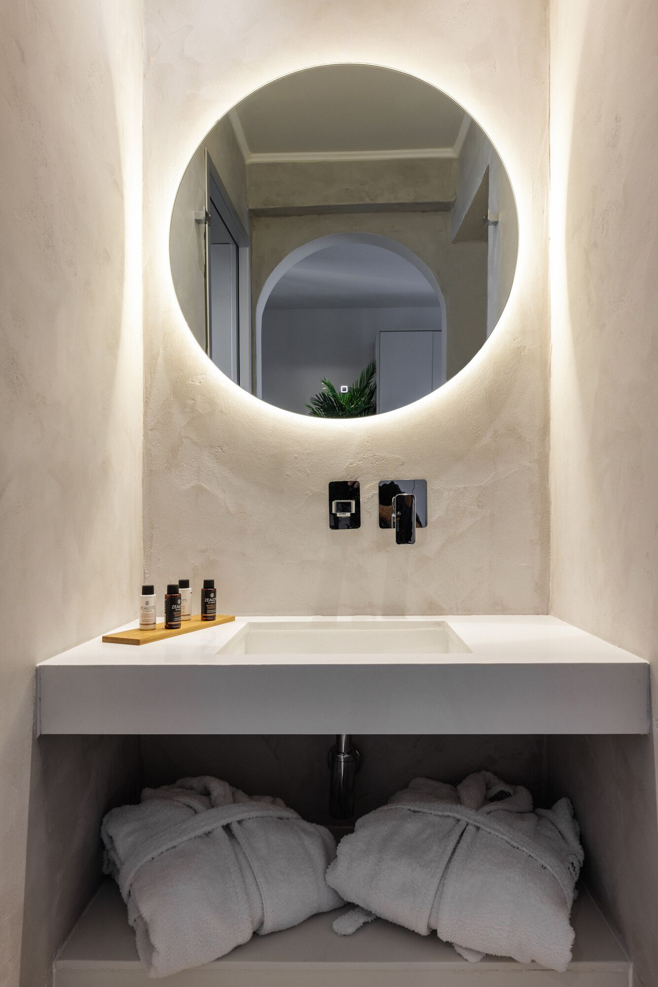 A bathroom with a white sink, a round mirror, and two towels on a shelf.