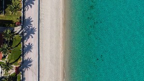 An aerial view of a beach with clear turquoise water, a sandy shore, and palm trees. - Amalthia Luxury Suites (Kassandra)