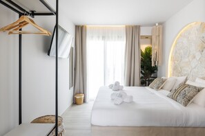 Quarto de hotel moderno com uma cama grande, um cabide de madeira, uma televisão e uma parede de detalhes em pedra.