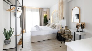A modern hotel room with a bed, a seating area, a mirror, and a plant. - Amalthia Luxury Suites (Kassandra)