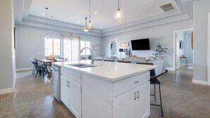 Une cuisine spacieuse dotée d’un grand îlot central, de luminaires suspendus et d’un coin repas avec des chaises et une table.
