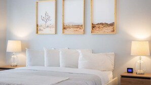 Une chambre d’hôtel avec un lit, du linge de lit blanc, deux lampes de chevet et trois tableaux encadrés accrochés au mur.