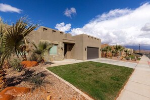 Una casa moderna con garaje, césped cuidado y jardinería de estilo desértico.