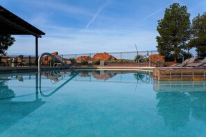 Una piscina cristalina con una escalera metálica, rodeada de sillas de descanso y una valla.