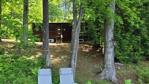 Eine rustikale Holzhütte, umgeben von dichtem Wald, mit einer Leiter, die zu einer Holzterrasse führt.