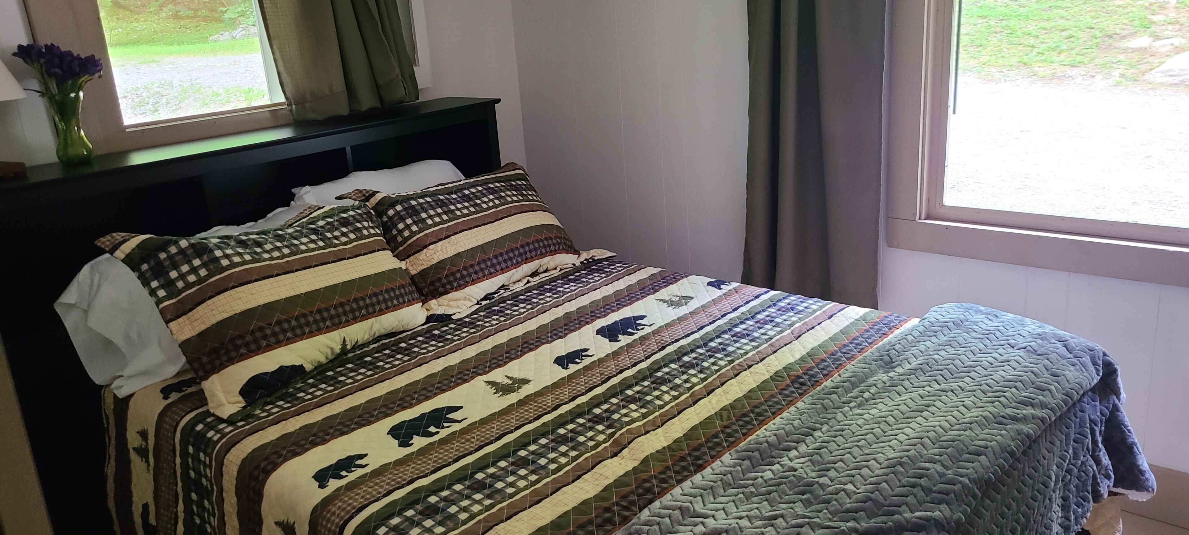 Ein Bett mit einer gestreiften Bettdecke und einem Bärenmuster, eine Vase mit Blumen und ein Fenster mit Vorhängen.