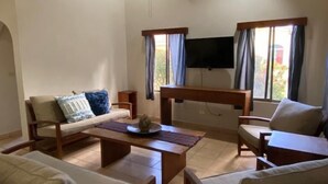 A living room with a ceiling fan, a flat-screen TV, and a large window with curtains. - Casa Dulce Vida Gran Pacifica Resort (Villa El Carmen)