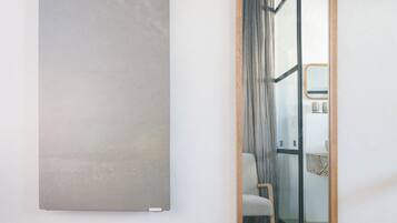 Un baño moderno con cabina de ducha de vidrio, una silla blanca y un cuadro abstracto grande en la pared.