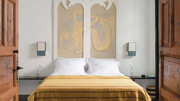 Un dormitorio con cama, puertas de madera, un cuadro abstracto grande, mesitas de noche e iluminación fijada en la pared.