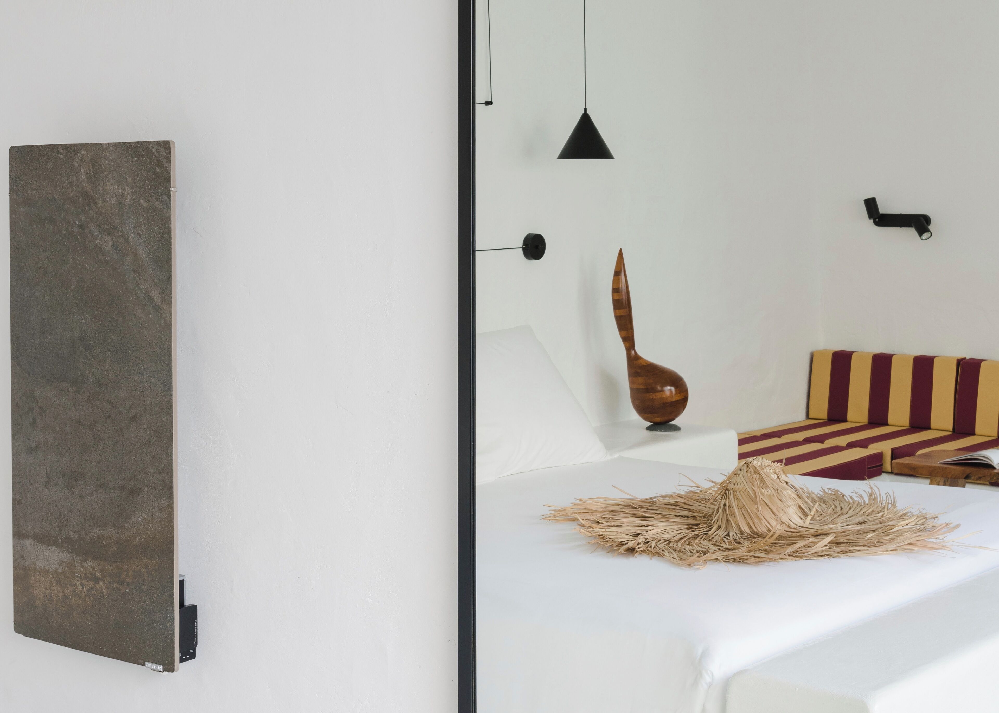 A modern bedroom with a large mirror, a bed with striped bedding, a hanging light, and a decorative wooden vase.
